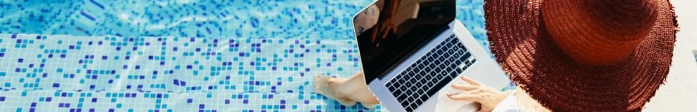 Woman using a laptop working remotely near a swimming pool.