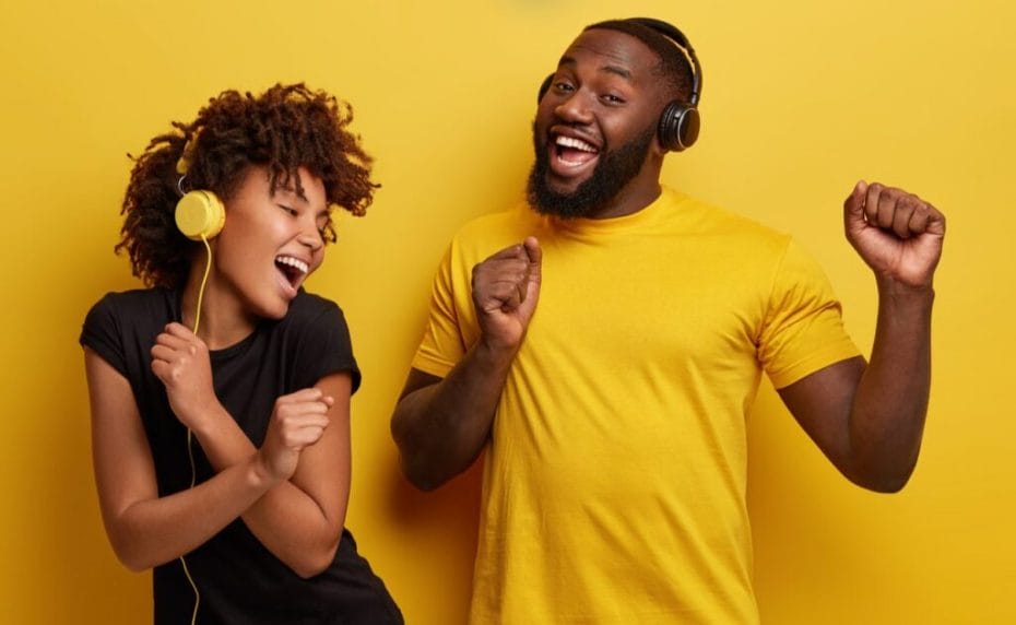 Two cheerful young people listening to music and dancing against a yellow background.