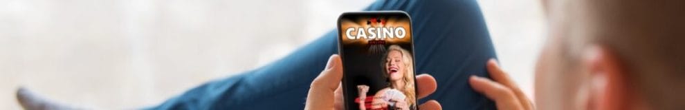 Man sitting on a couch holding his phone with a casino-themed background on the screen.