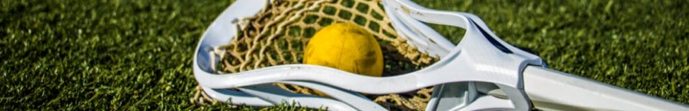 Yellow ball and lacrosse stick lying on a green playing field.