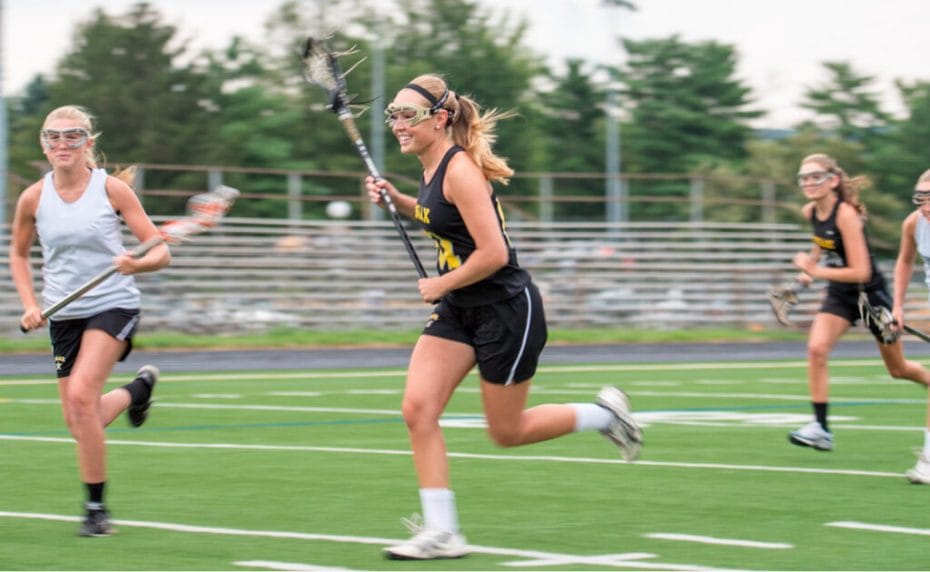 Opposing teams run across a playing field during a girls’ lacrosse game.