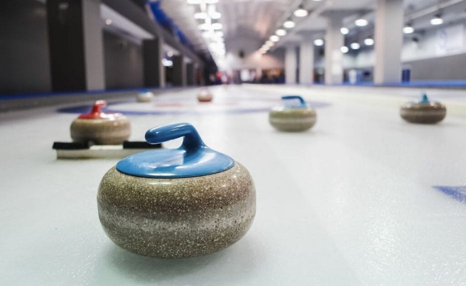 Curling stones lined up on the ice playing field.