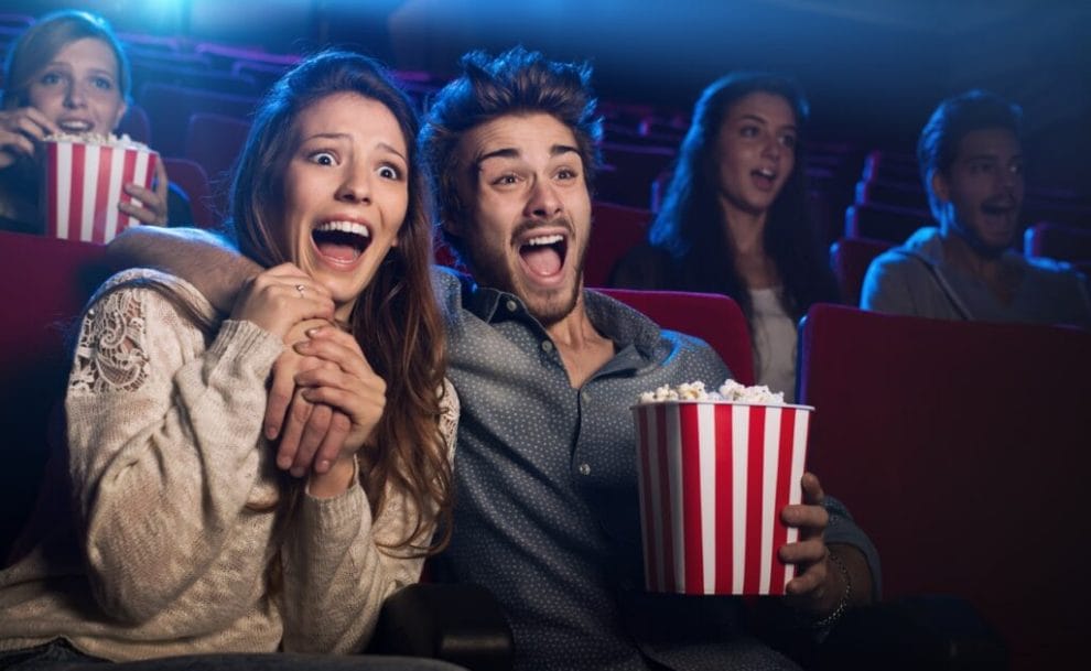 Young couple laughing while watching a cinema movie and eating popcorn.