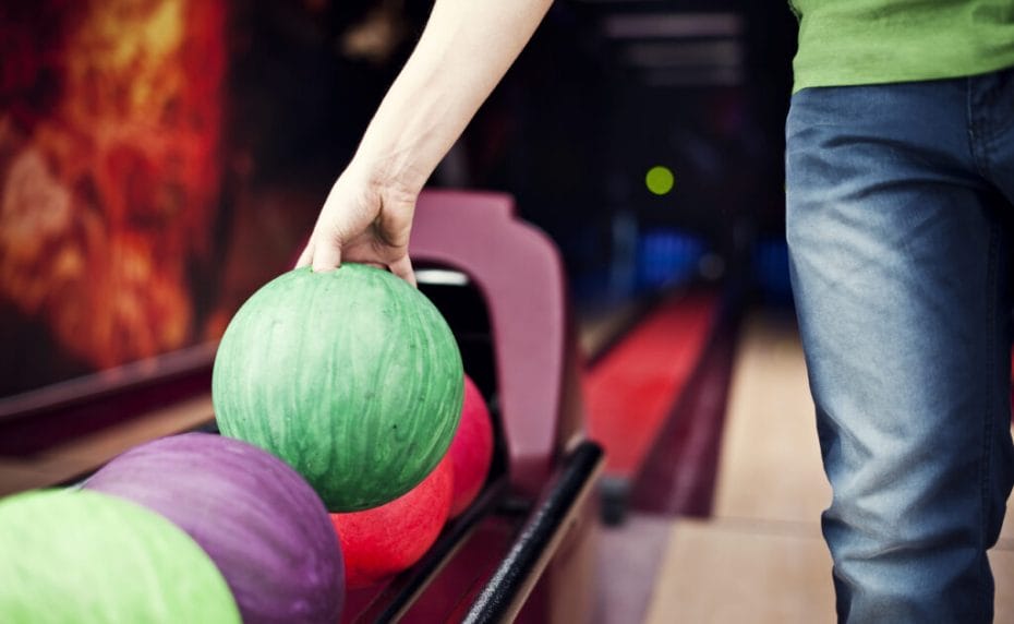 Someone picks up a green bowling ball from the conveyor belt at a bowling alley.