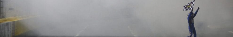 Stock car racing driver Kyle Busch waves a checkered flag in the air.