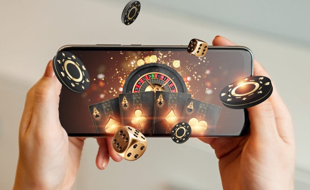 Dice and casino chips tumbling from a smartphone screen that displays playing cards and a roulette wheel.