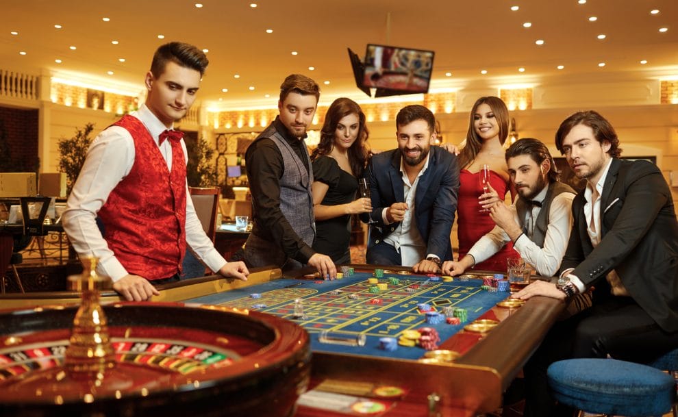 Group of happy people placing bets on roulette at a casino table.