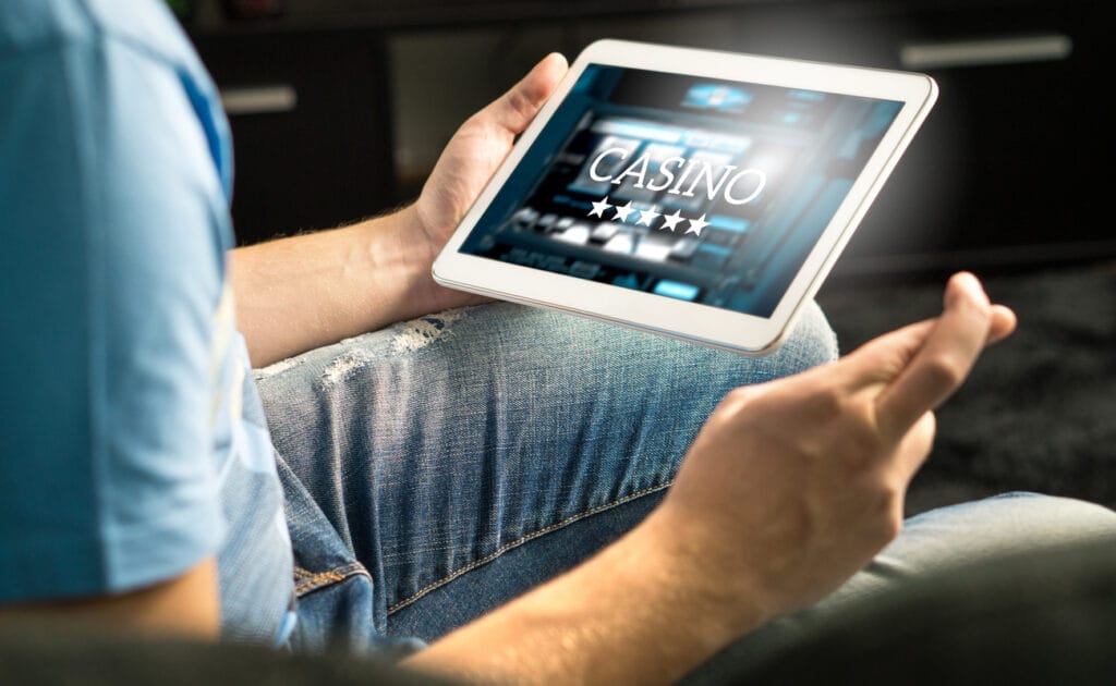 Man in blue jeans crosses his fingers while playing casino games on his laptop.