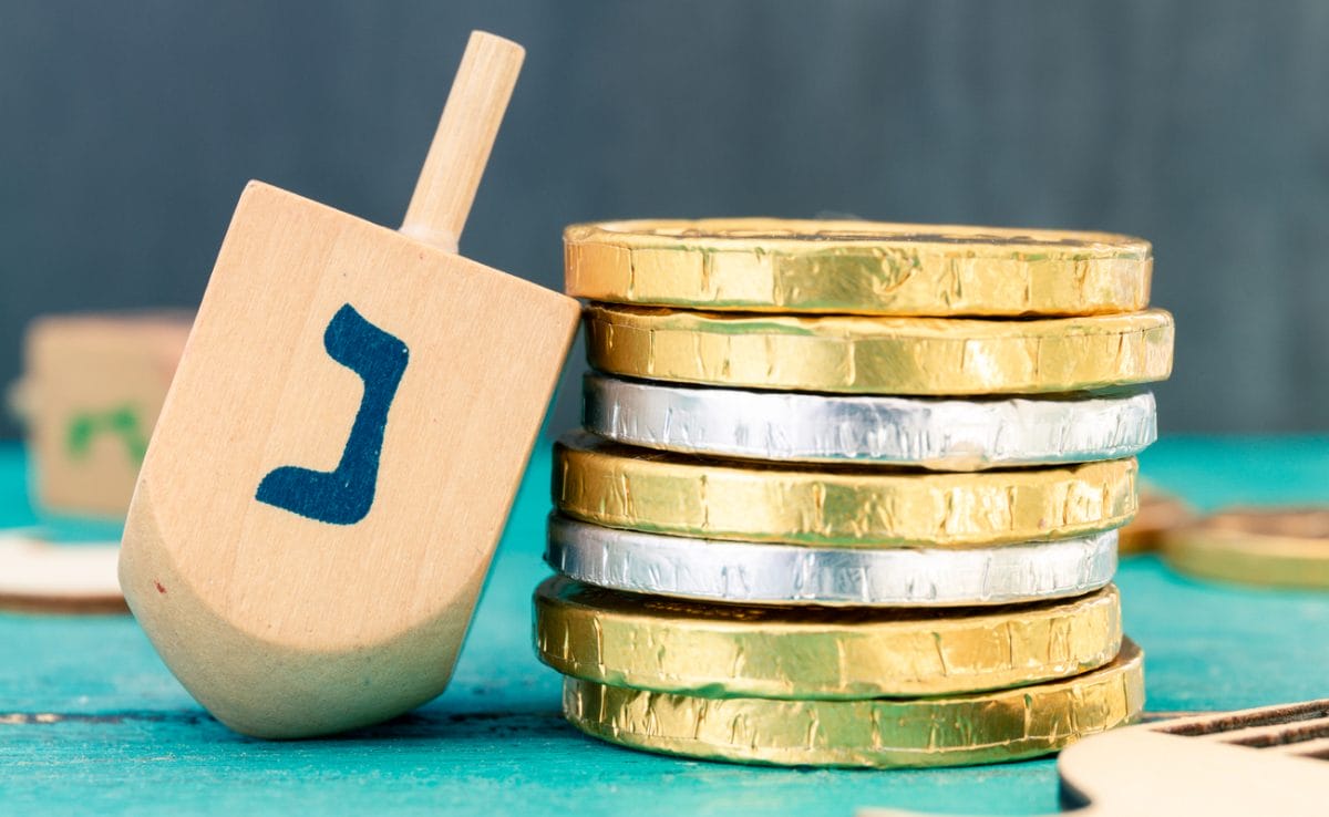 A dreidel spinning top next to a stack of gold- and silver-foiled chocolate coins.