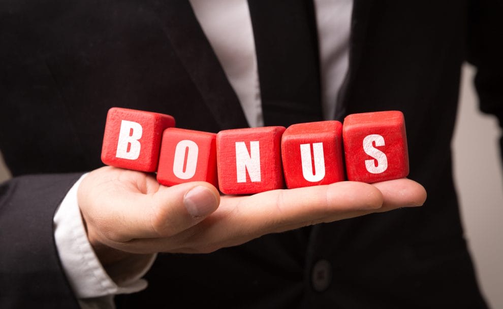 A man in a dark suit holds in the palm of his hand red blocks that spell out ‘bonus.’