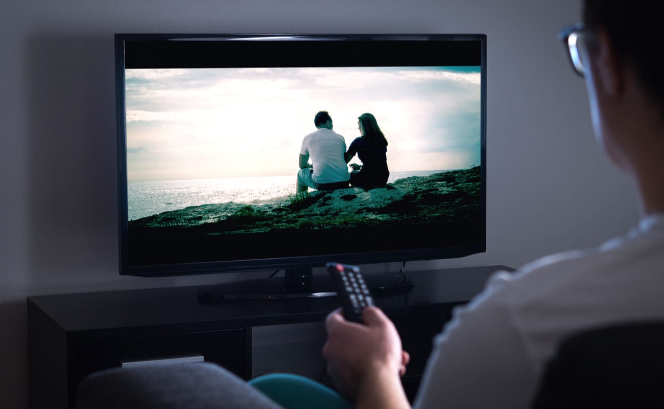 A man holding a remote watches TV.