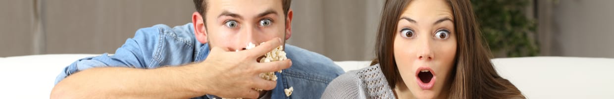 A couple looks amazed watching TV and eating popcorn.