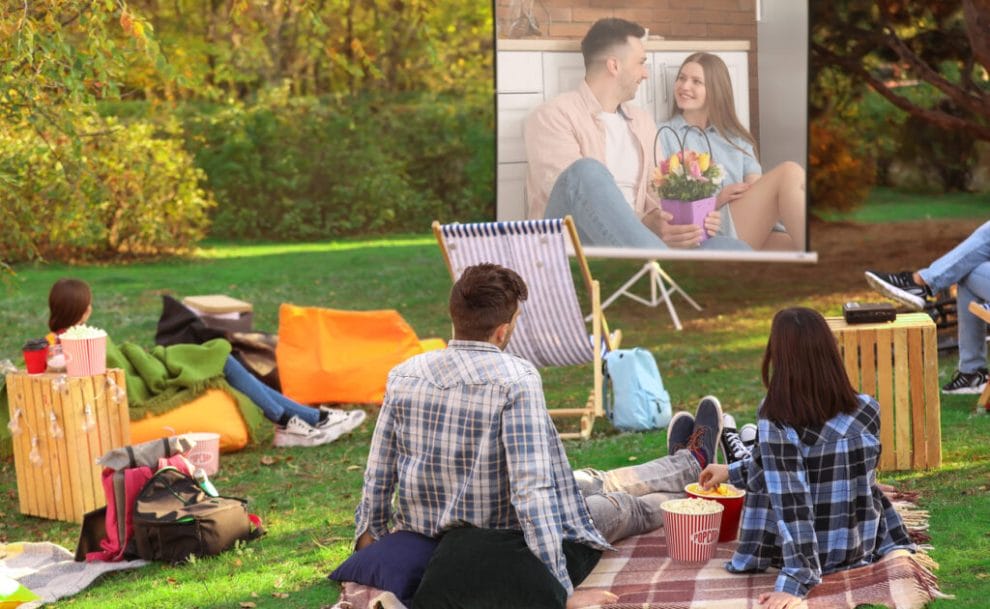 Friends sitting on rugs on the grass at an outdoor movie house party.