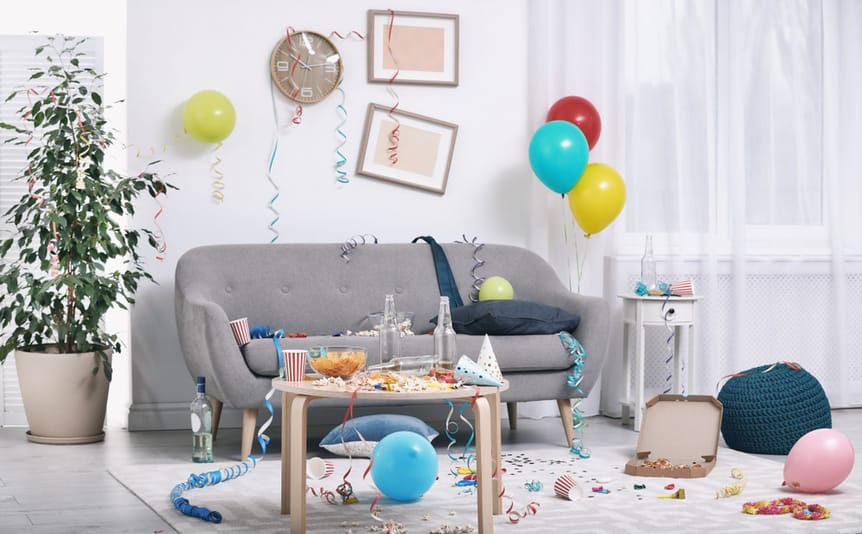 Snacks, drinking cups, and streamers left on a gray couch after a party.