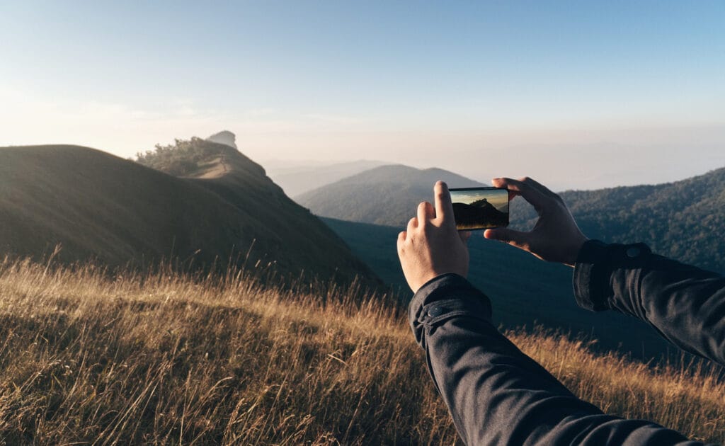 A person takes a picture of hilly landscapes on their phone.