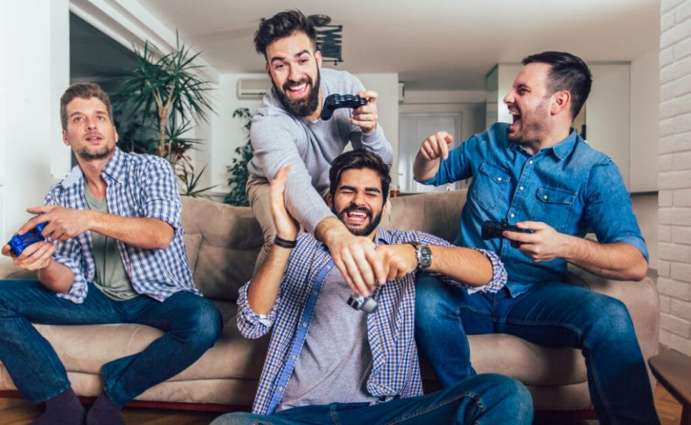 Male friends laughing and having fun playing video games on a couch.