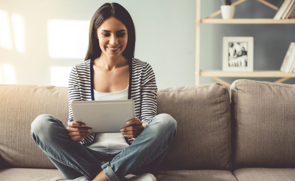 A woman sits on her couch playing online bingo on her tablet.