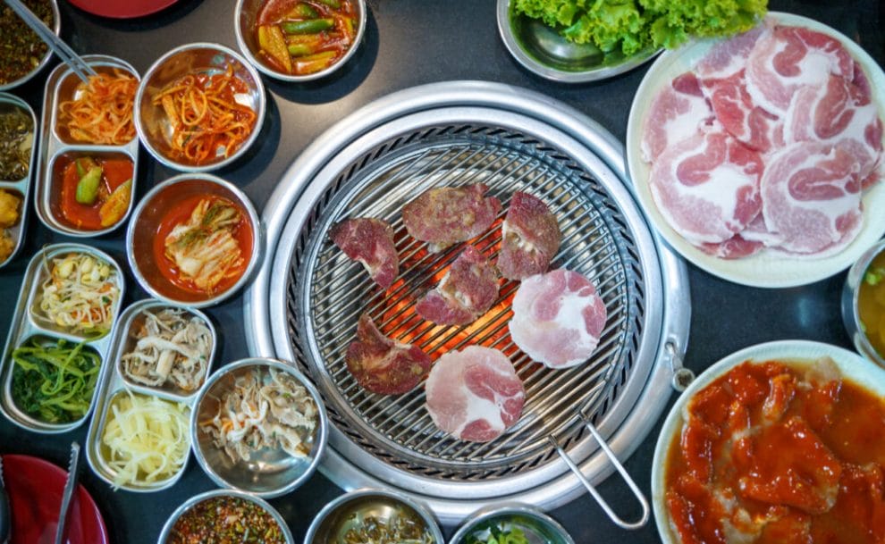 Top view of a Korean BBQ with an assortment of meat on the grill and sides on the table.