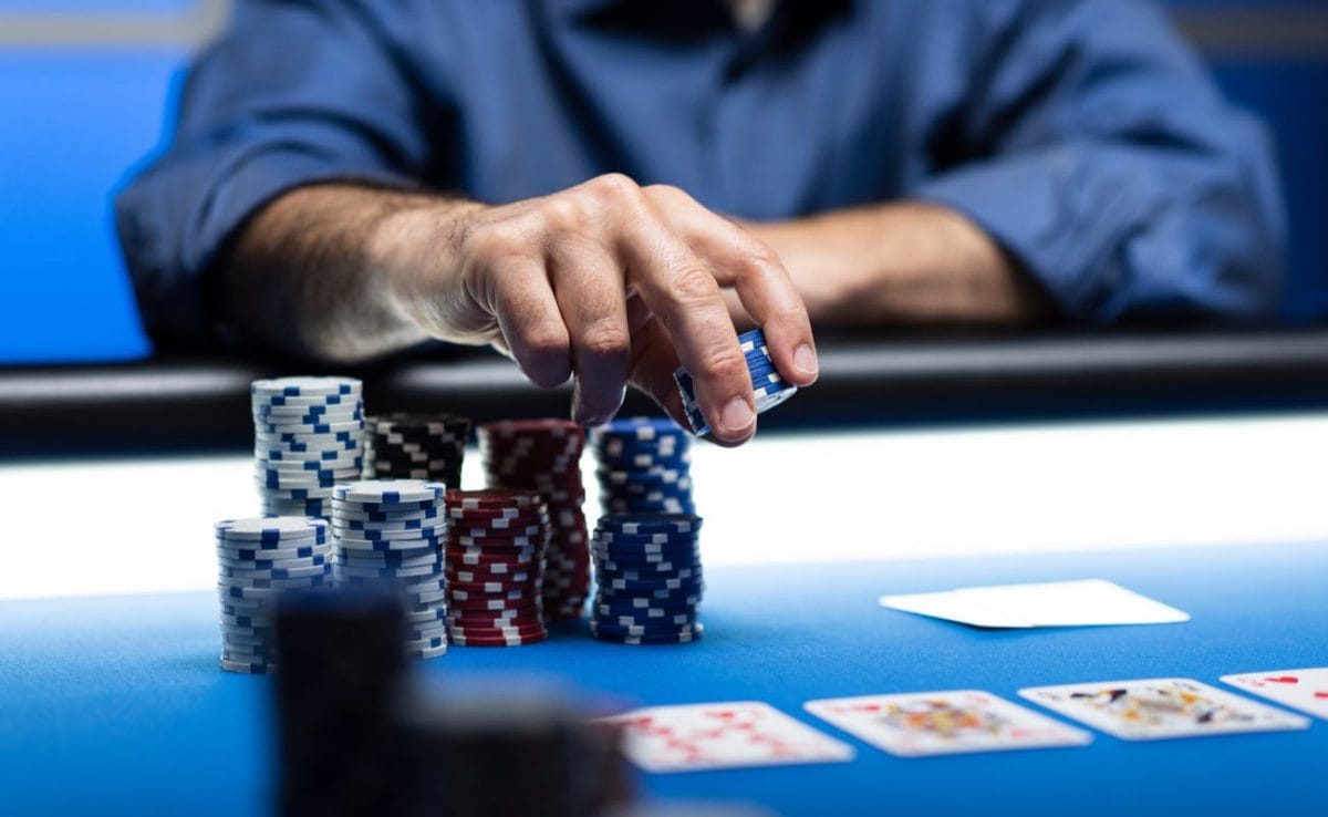A man reaching for a stack of casino chips with playing cards revealed on the table.
