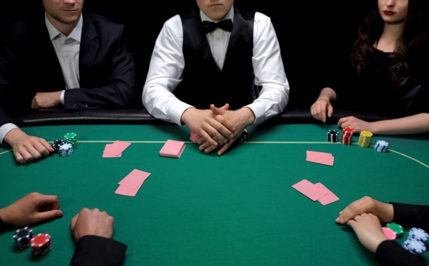A group of people sitting around a green poker table with cards and chips on the table.
