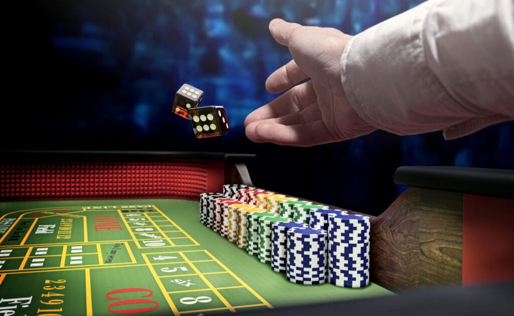 A dealer throws dice onto a craps table next to a stack of chips.