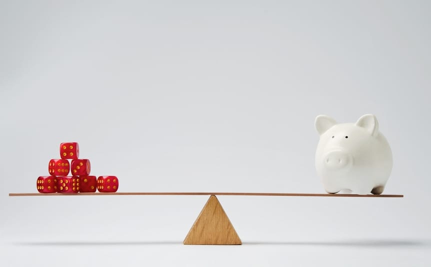 Balanced wooden seesaw with dice on one side and a piggy bank on the other against a white background.