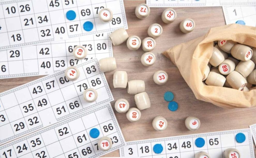 Table full of 90-ball bingo tickets, a bag full of wooden barrels with numbers on them and blue markers