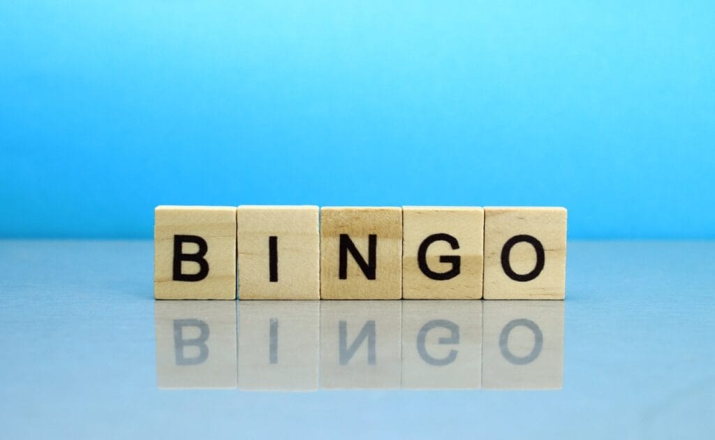 Wooden blocks spelling out the word bingo on a reflective surface with a blue background.