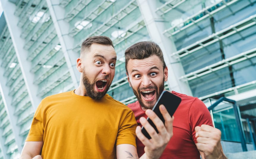 Two excited men looking at a phone shouting and celebrating.