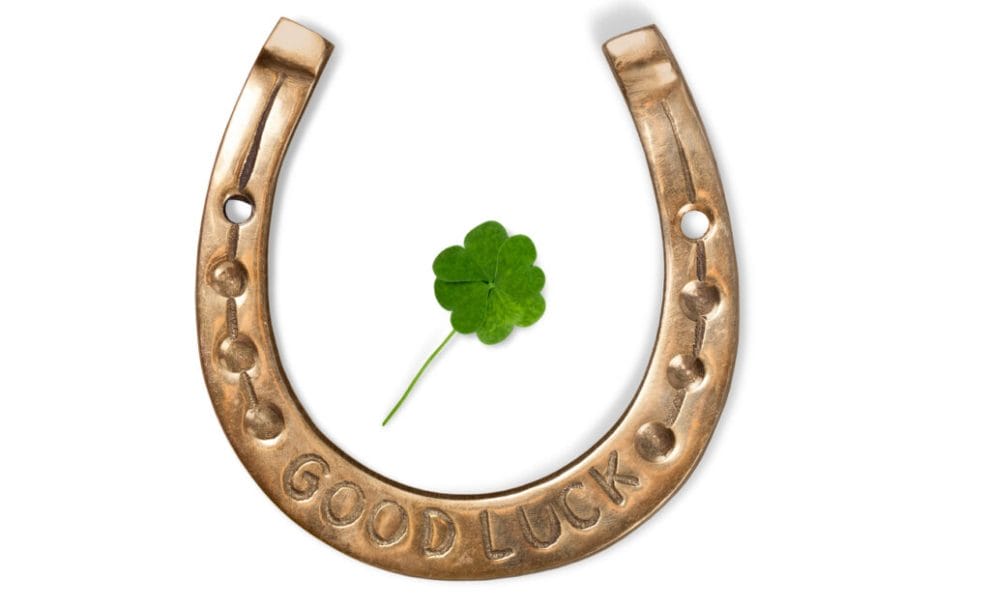 A horseshoe with a “good luck” engraving and a four-leafed clover in the middle on a white background.
