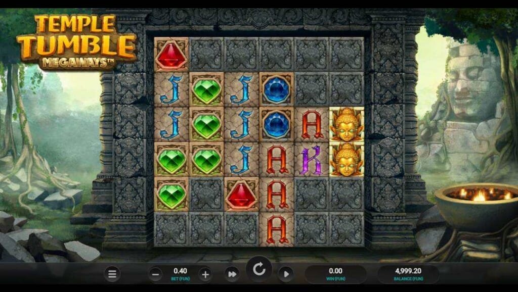 A screenshot of the slot reels in Temple Tumble Megaways. The setting is the ruins of an ancient civilization in a jungle. The reels are set in the crumbling walls of the ruins and feature gems, masks, and playing card symbols.