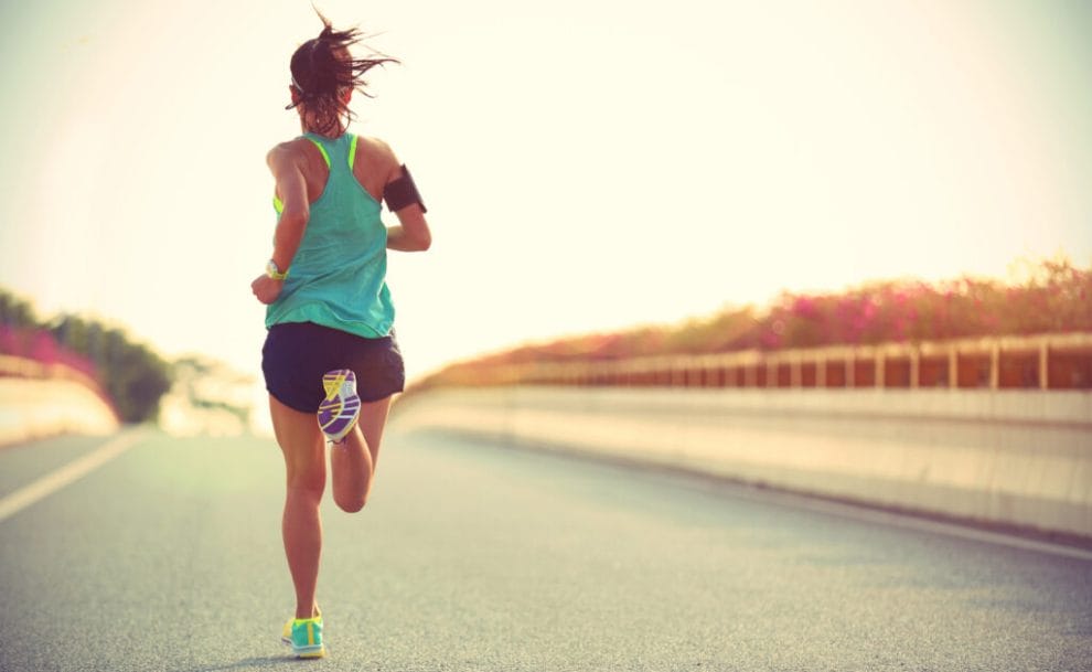 A woman runs on a tar road over a bridge in the sunset.