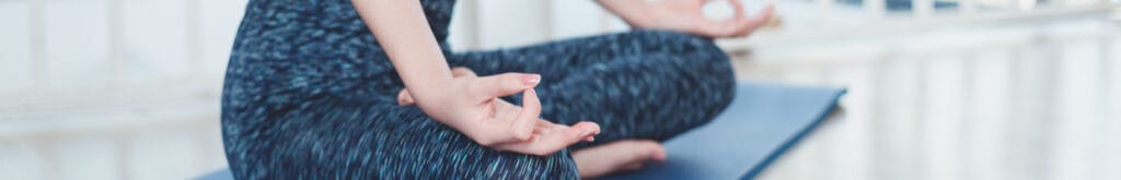 A young woman in a yoga pose with legs crossed and hands facing upwards with her index finger and thumb touching.