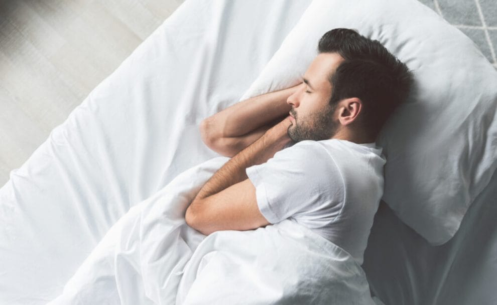 A young man sleeping on his side with his hands under his head.