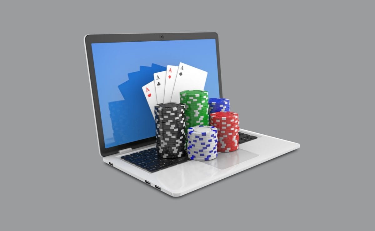 Casino chips and playing cards on top of an open laptop against a gray background.