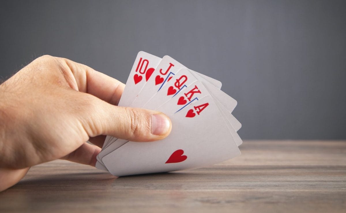Hand holding a royal flush of cards on a wooden table.