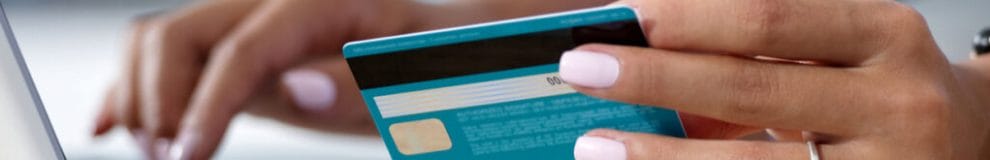 A woman holding a blue bank card typing on a laptop keyboard.