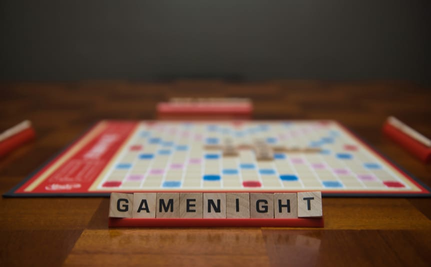 Letter tiles spelling out the words “game night” on the stand in the foreground with a game board in the background.