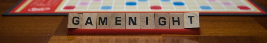 Letter tiles spelling out the words “game night” on the stand in the foreground with a game board in the background.