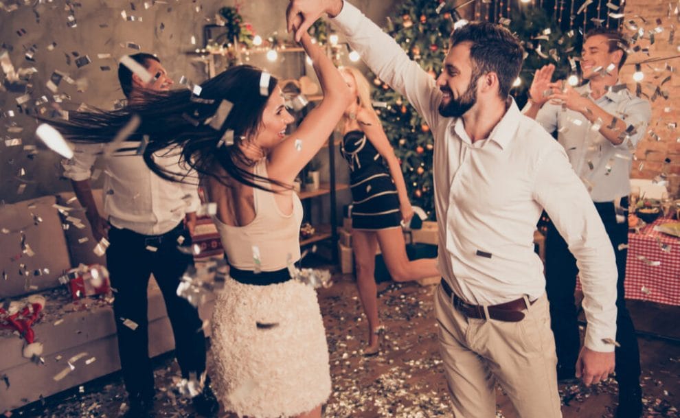 A couple of friends in smart casual clothing dance in the lounge with confetti in the air.