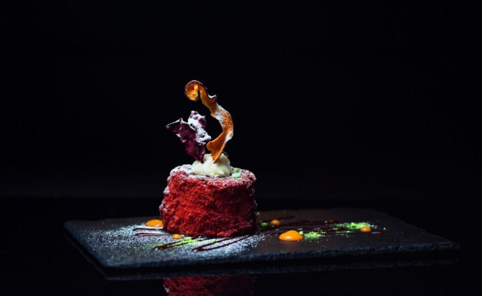 A beautiful, well-constructed dessert on a black slate board with a dark background.