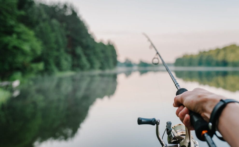 A person holding a fishing rod casting out into a lake.