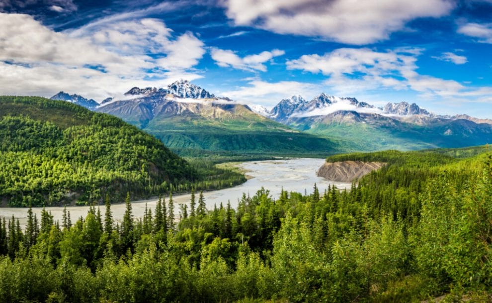 The Chugach mountain range in Alaska with a river and forest in the foreground.