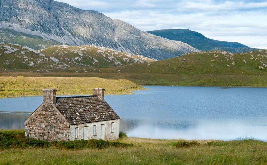A small remote stone house in front of a lake.