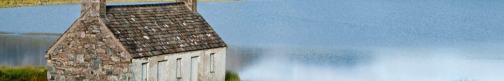 A small remote stone house in front of a lake.