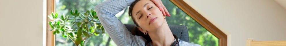 A woman stretches her neck with her hand while sitting at a desk.