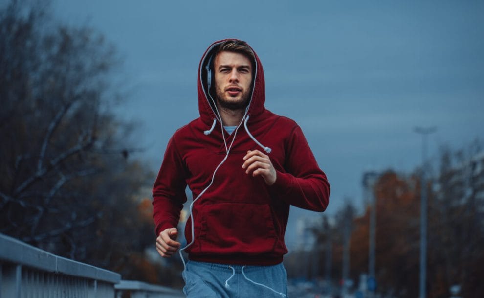 A man runs in the evening with headphones and a hoodie on.