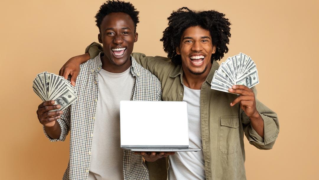 Two men holding cash, one putting the arm around the other, who is holding a laptop.