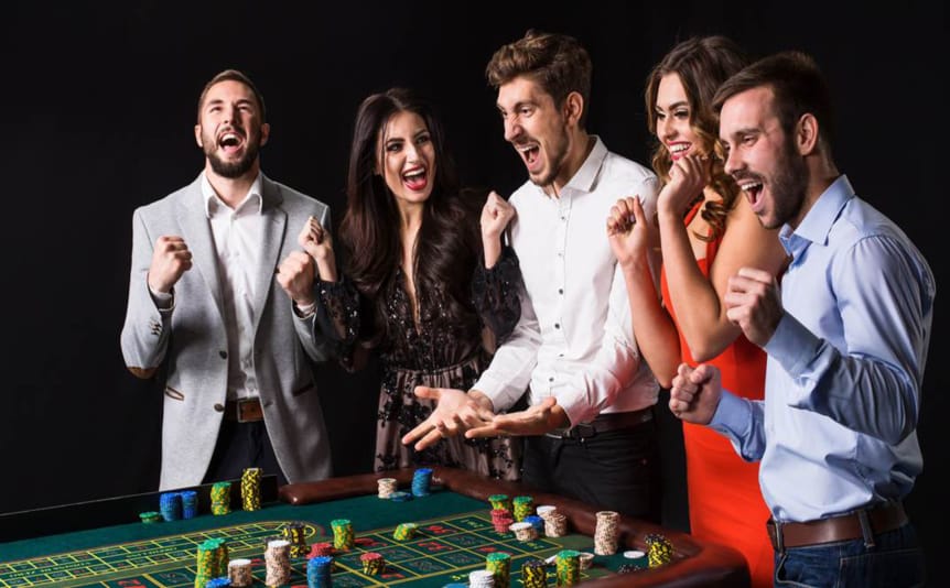 Group of people standing at a roulette table and shouting excitedly.