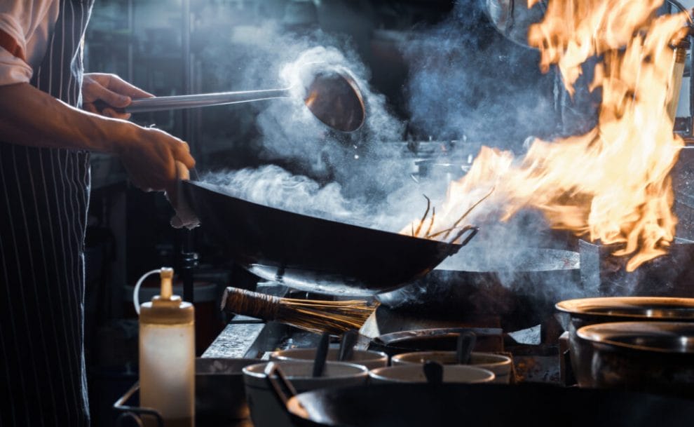 A chef pours liquid into a pan with a ladle.
